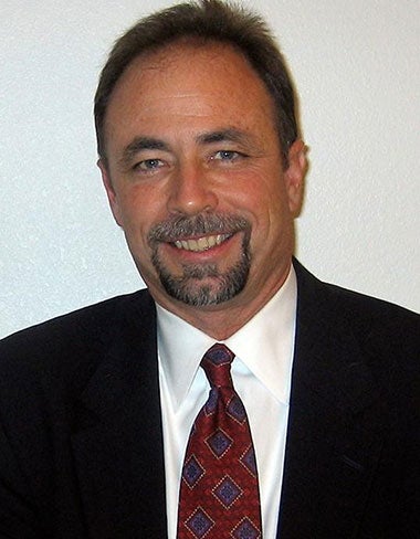 A man in a suit and tie smiles confidently at the camera, showcasing a professional appearance.