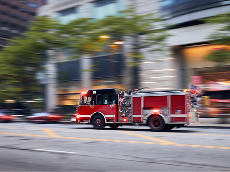 A fire truck driving down a city street, with lights flashing and sirens blaring, responding to an emergency call.