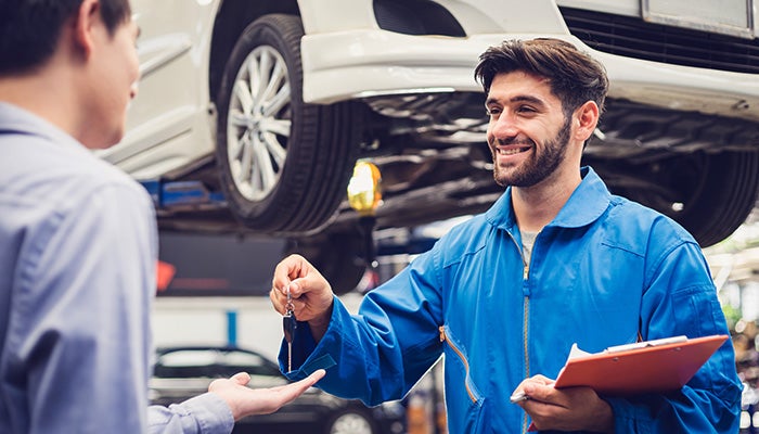 A man speaks with another man inside a car repair shop, surrounded by tools and car parts.